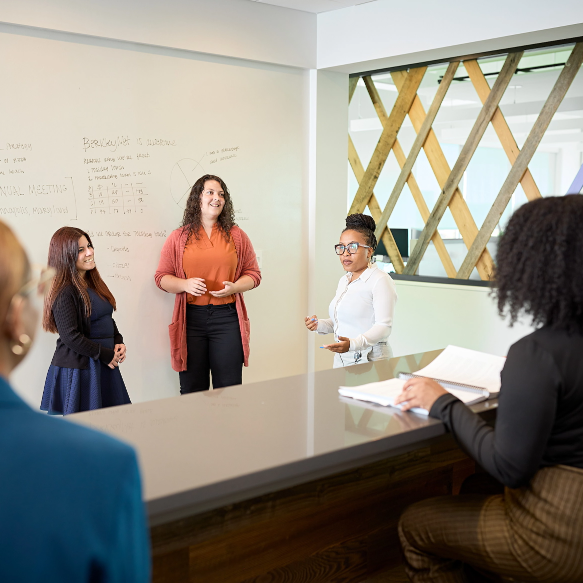 WC Policy Premium Audit Three BerkleyNet employees presenting in front of a whiteboard, speaking about conducting a workers compensation insurance policy premium audit.