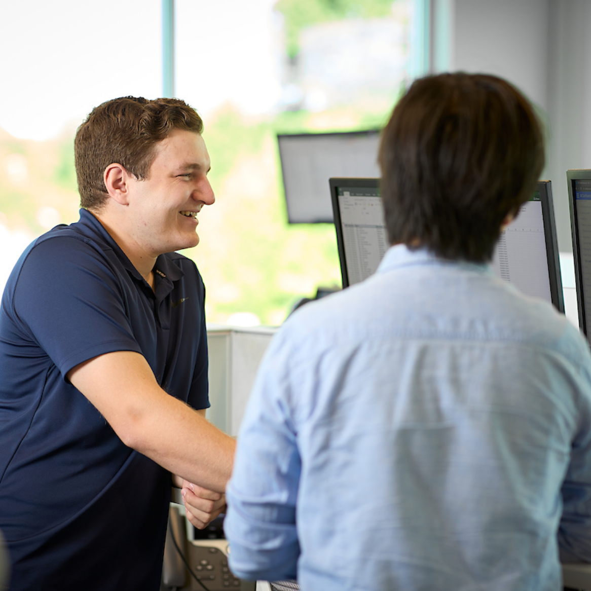 Workers comp insurance jobs at BNet Two BerkleyNet employees smiling while reviewing workers compensation insurance on monitors in an office, a positive workplace culture and team spirit for careers in workers compensation insurance industry.