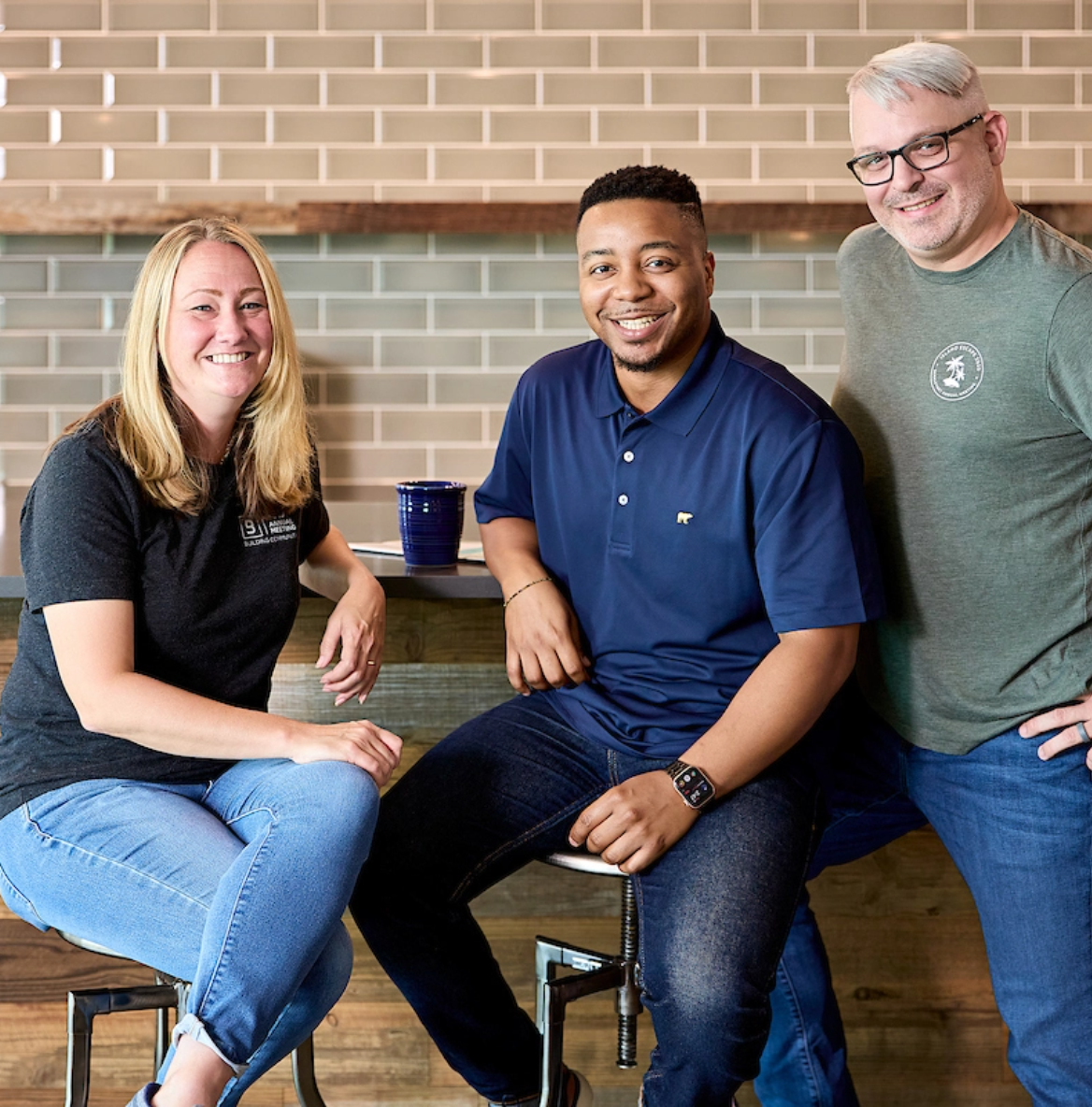Workers comp insurance providers who we are Three smiling BerkleyNet employees standing in the office café with a positive workplace culture and a team committed to fast workers compensation insurance solutions.