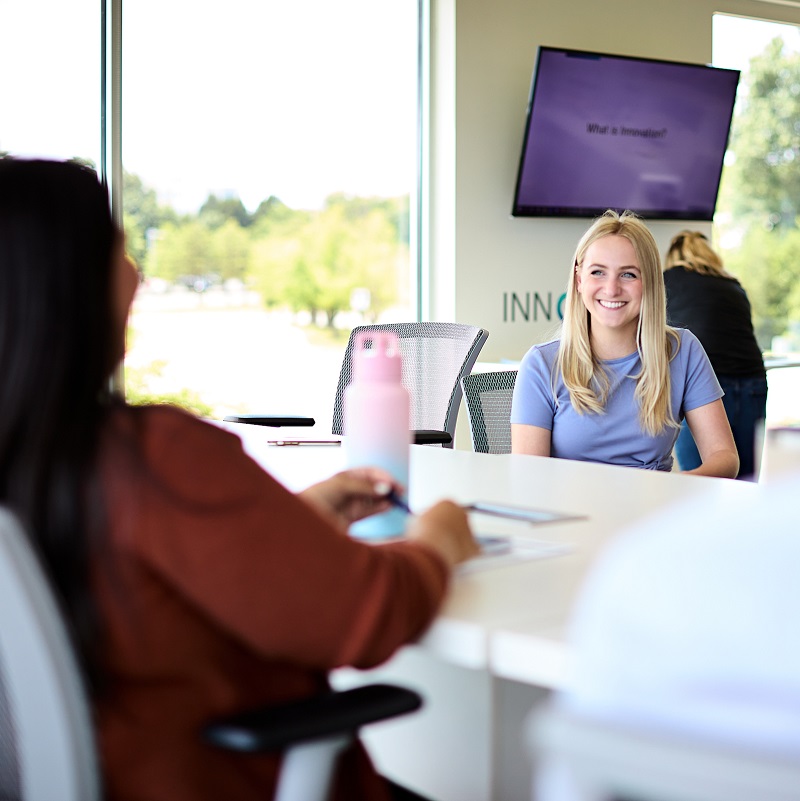 Workers comp insurance companies claims excellence Two BerkleyNet employees at a desk in an office; one smiling brightly in the 'Innovation' workspace, reflecting a creative and fast culture for workers compensation insurance.
