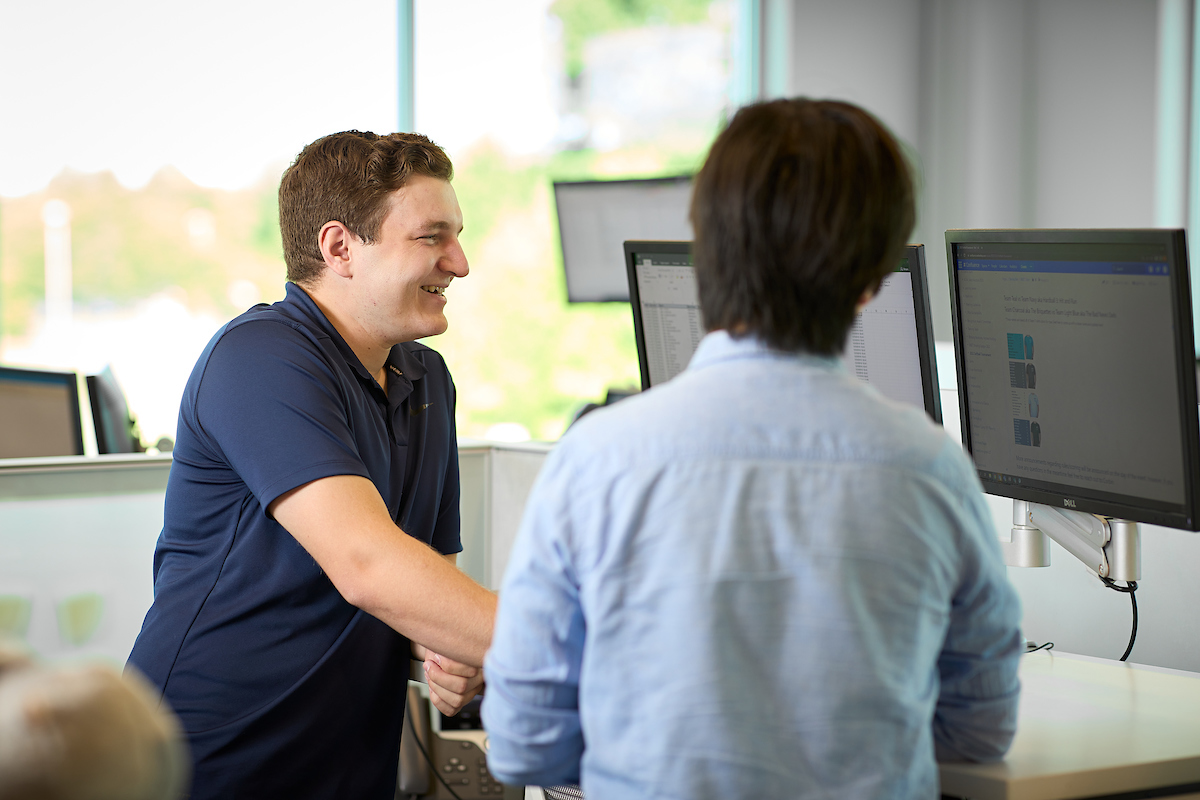 Easy Claim Reporting and Why it Matters Two BerkleyNet employees smiling while reviewing workers compensation insurance data on monitors in an office.