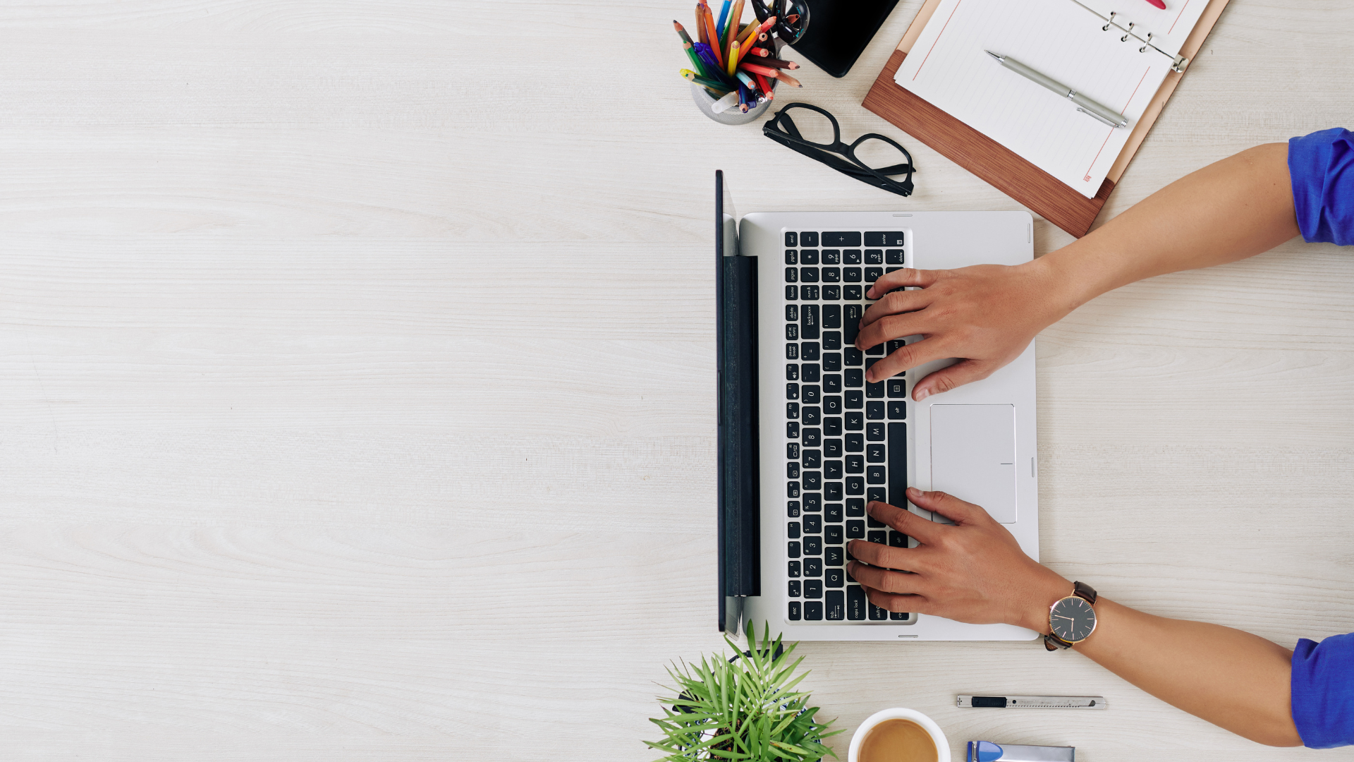Overhead view of a person typing on a laptop at a desk with office supplies, representing payroll reporting plans in workers compensation insurance. 