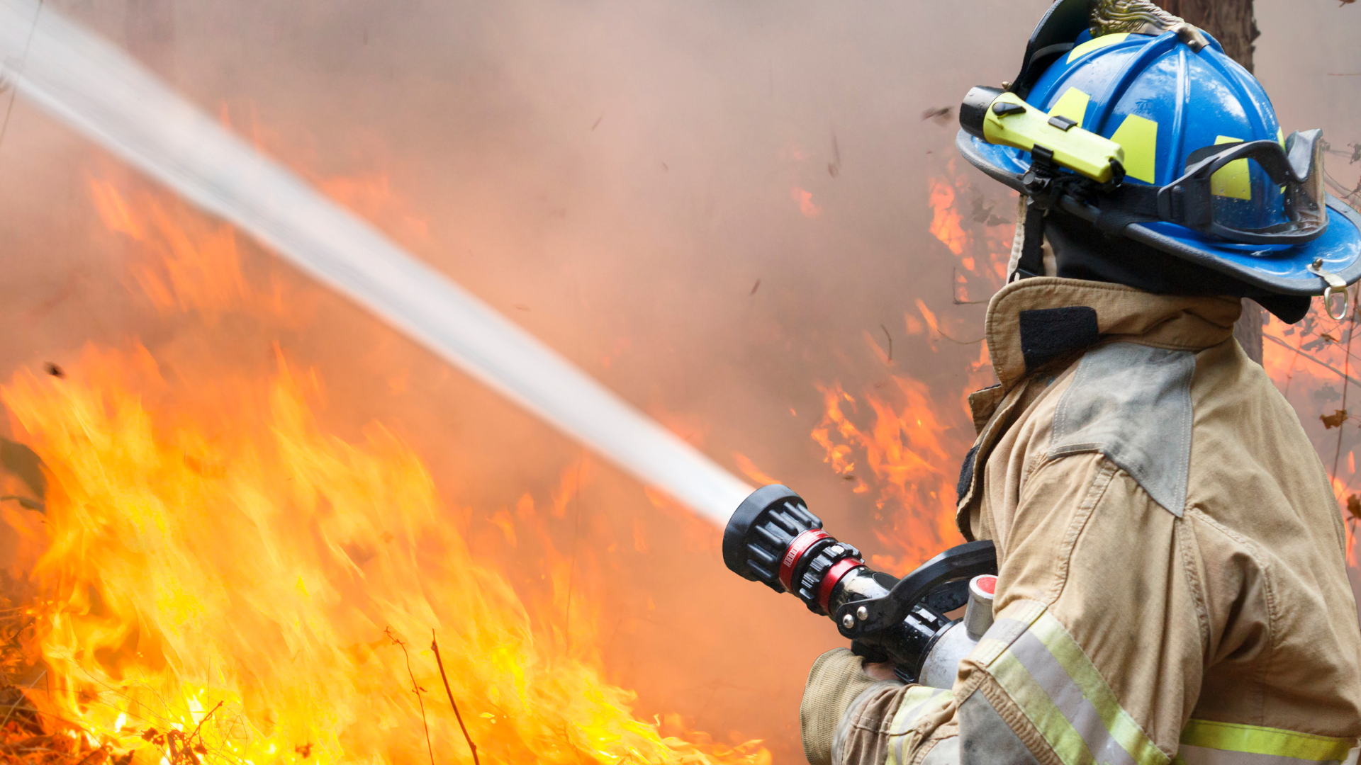 Back view of a firefighter using a hose to extinguish a fire, representing California fire restoration efforts and the importance of proper workers compensation insurance coverage. 